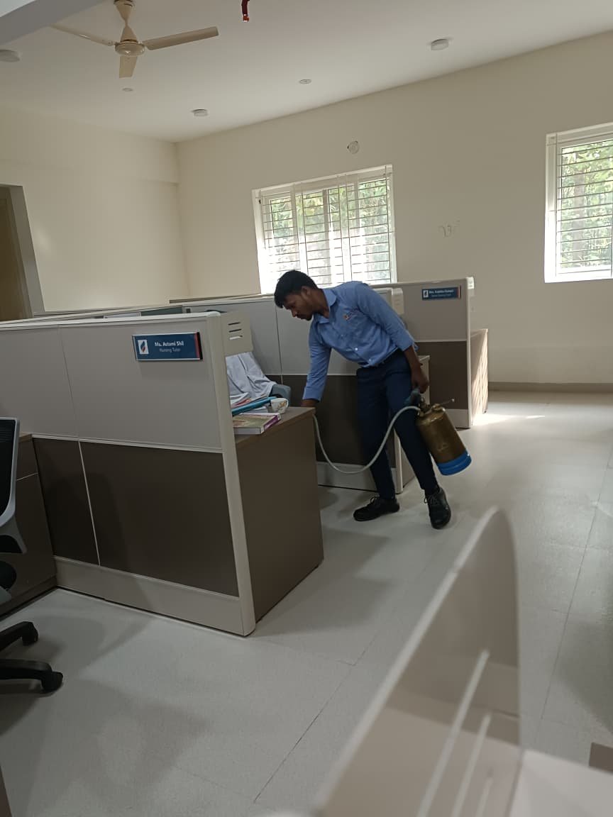 Technician spraying pest treatment near office workstations