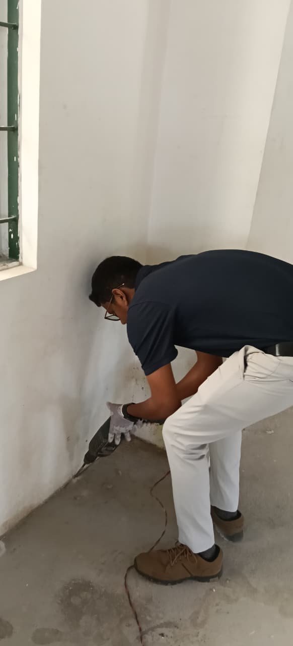 Technician spraying pest treatment along a wall corner